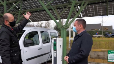 un barbat arata catre panourile solare ale unei statii de incarcare pentru masini electrice