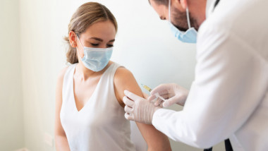 O tânără este vaccinată de un cadru medical.
