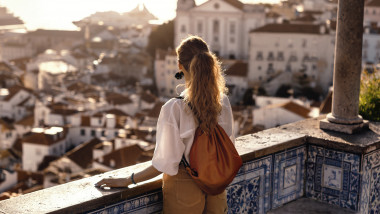 femeie cu rucsac care priveste dinr-un balcon perspectiva unui oraș
