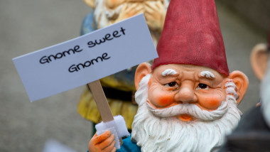 pitic de grădină care tine în mana o pancardă pe care scrie gnome sweet gnome
