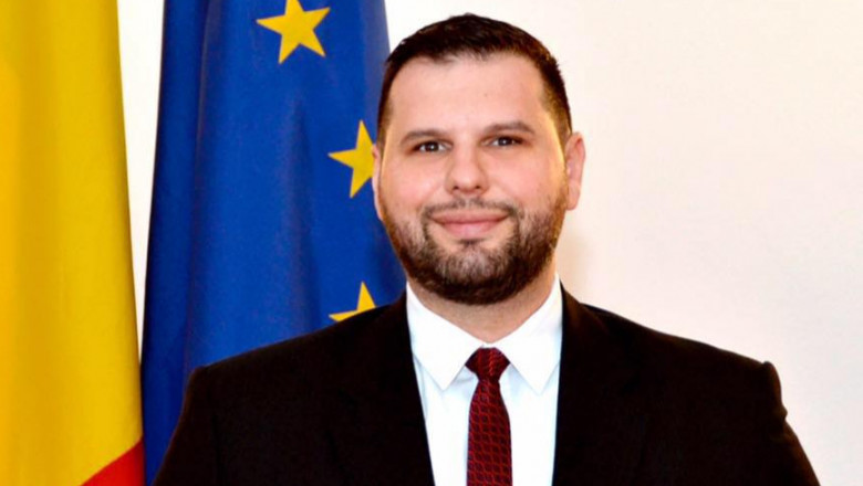 Dan Stoenescu lângă drapelele României și Uniunii Europene.