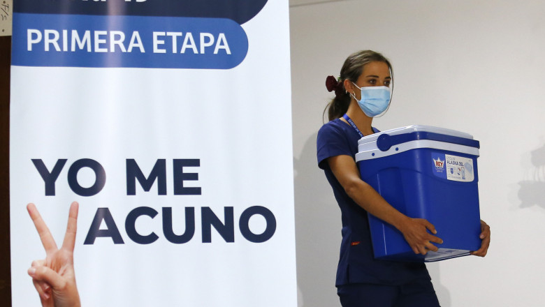 un cadru medical cara o ladă frigorifica cu vaccinuri trecand pe langa un panou pe care scrie in spaniola „eu ma vaccinez”