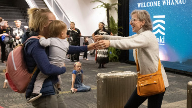 O femeie cu brațele întinse spre fiica și nepotul ei pe aeroportul din Wellington. F