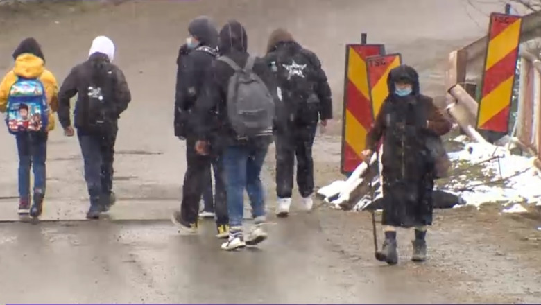 copii care merg la scoala pe un drum de tara in timp ce ploua