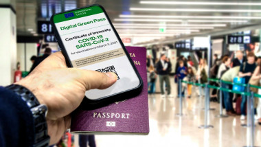 O persoană ține în mână un telefon cu pașaportul digital de vaccinare și un pașaport