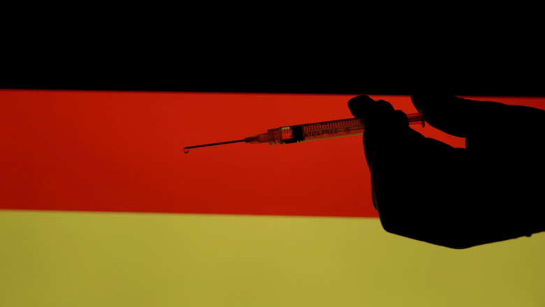 o mana cu o seringa de vaccin, pe fundal steagul germaniei