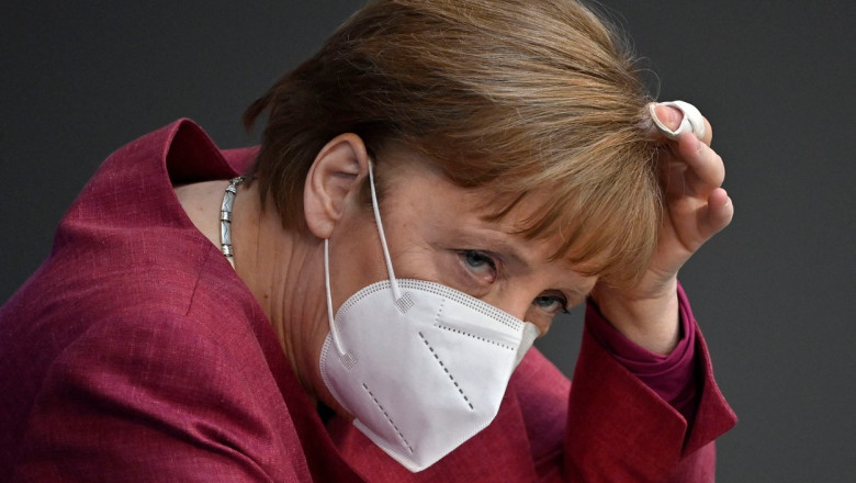 Angela Merkel, cu mască, își ține mâna în păr.
