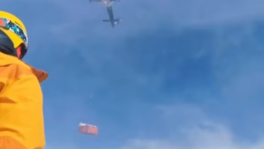 un barbat supravegheaza un elicopter care transporta materiale de constuctii