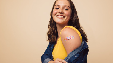 Tanara zambeste in timp ce isi arata umarul unde are un plasture in urma vaccinarii