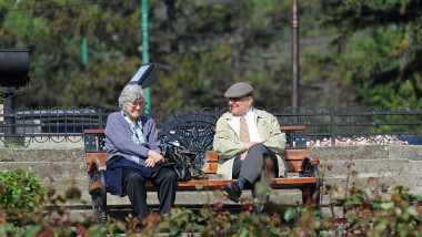 Doi pensionari stau pe bancă, într-un parc.
