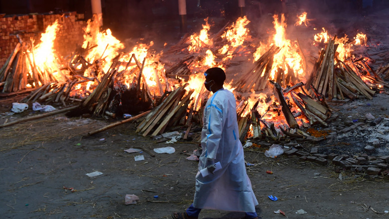 un barbat imbracat in combinezon trece pe lângă niște crematorii improvizate unde ard cadavre