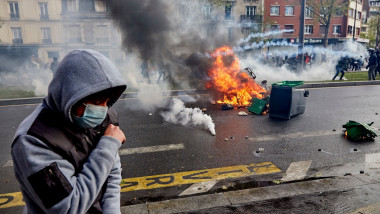 Protestatar cu mască se ține de umăr în timp ce un incendiu arde pe fundal
