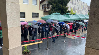 Zeci de oameni cu umbrele așteaptă în ploaie să se vaccineze împotriva COVID-19 în Blaj, județul Alba.