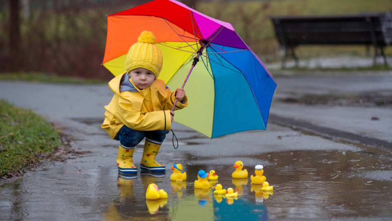 copil cu umbrela care se joacă cu ratuste in ploaie