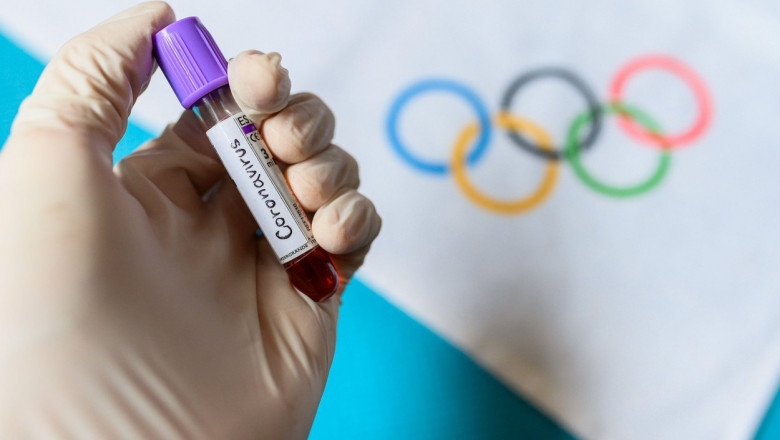 epubreta tinuta intr-o mana cu manusa pe fundal cercurile jocurilor olimpice