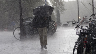 un barbat cu umbrela merge prin ploaia torentiala