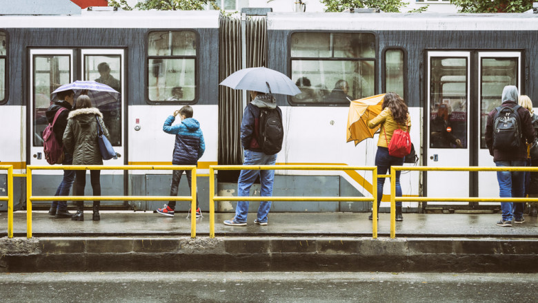 oameni cu umbrele in fata unui tramvai oprit in statie