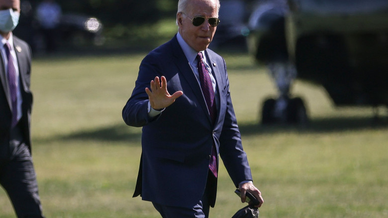 președintele american joe biden face semn cu mana in timp ce merge pe peluza casei albe