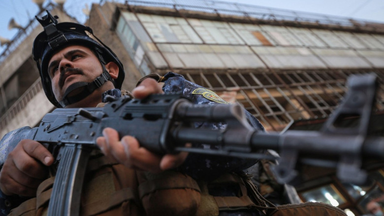soldat irakian care tine in mana o armă iar in spatele său se vede o clădire