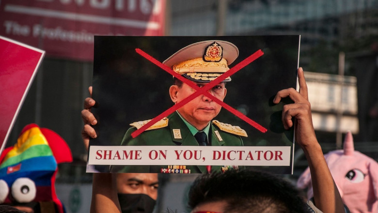 Bărbat cu o fotografia a dictatorului din Myanmar pe care este scris un x cu roșu cu mesajul „shame on you dictator”