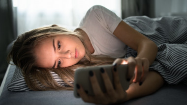 fată stă întinsă în pat și folosește smartphone-ul