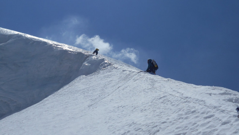 doi alpinisti in varf de munte cu zapada alba si cer senin
