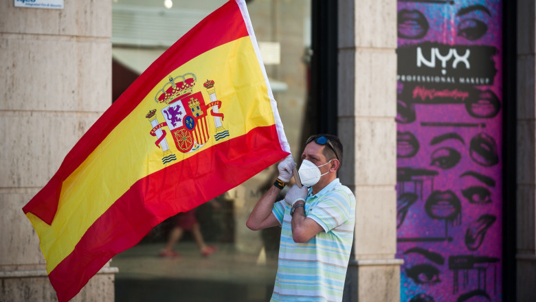 barbat cu masca pe strada care flutura steagul spaniei