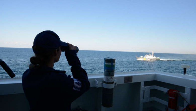 Un ofițer al marinei americane observă prin binoclu o navă iraniană.