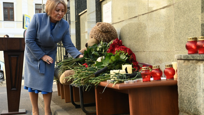 o femeie depune o floare la un altar improvizat cu flori si un urs de plus