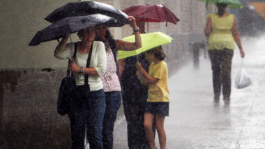 oameni pe stradă ferindu-se de ploaie sub umbrele