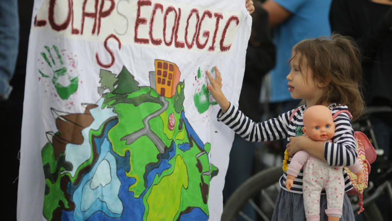 o fetită care tie în mana n bebelus de jucărie se uita pe un afis desenat cu teme ecologice