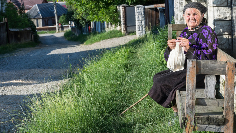 o femeie in varsta sta pe banca si croseteaza intr-un sat din romania