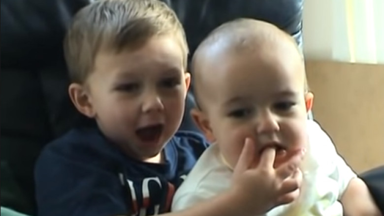 un bebelus il musca de deget pe fratele sau mai mare, care tipa de durere