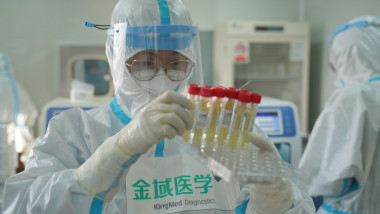 cercetator chinez intr-un laborator tinand in mana câteva eprubete cu lichid in ele