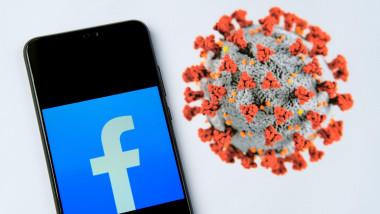 Telefon cu simbolul Facebook pe ecran și o reprezentare 3D a coronavirusului