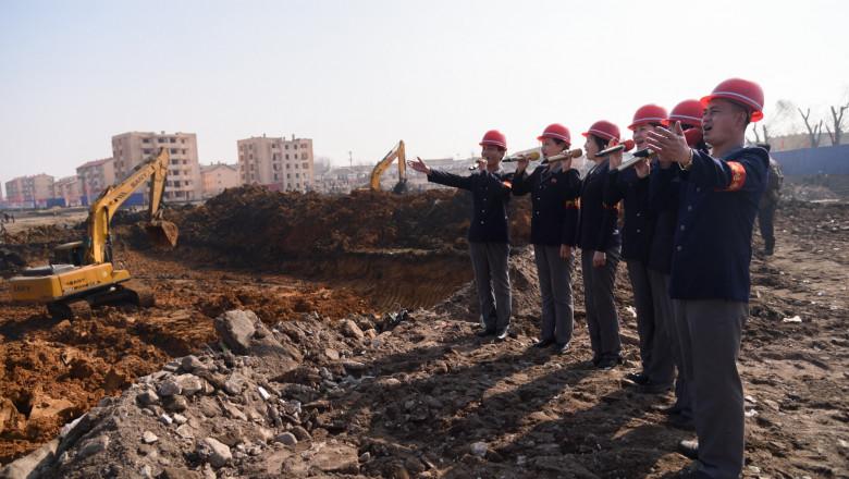 nord coreeni cu casca pe cap si microfon cante pe santier despre constructia de locuinte