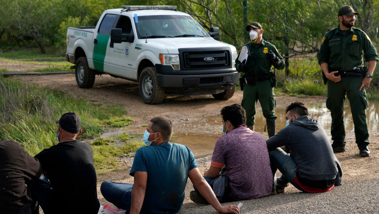 Migranți supravegheați de poliția de frontieră din SUA, la granița cu Mexicul.