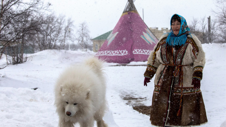 o femeie de la cercul arctic rus, in fata unei iurte, in zapada, langa un caine care seamana cu un urs polar