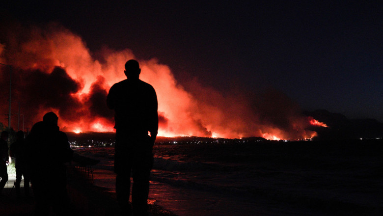Un bărbat privește la un incendiu de amploare izbucnit la aproximativ 70 de kilometri de Atena.