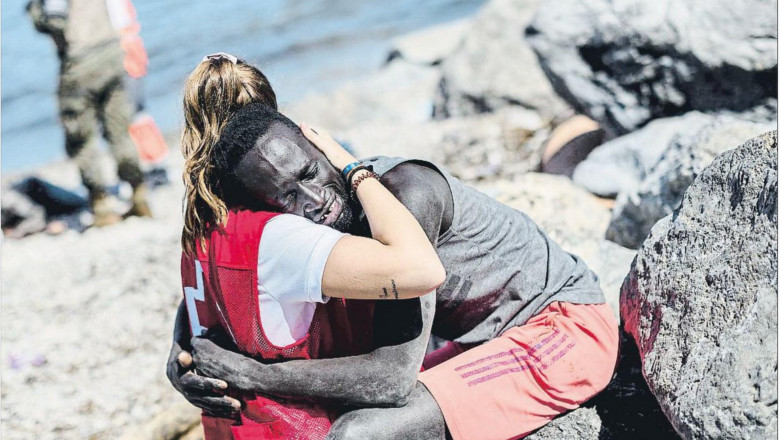 o voluntara de la crucea rosie imbratisează un migrant e culoare
