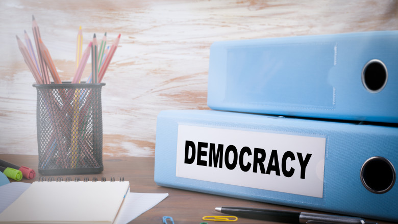 birou cu hartie, instrumente de scris si doua dosare groase pe cre scrie „democratie”