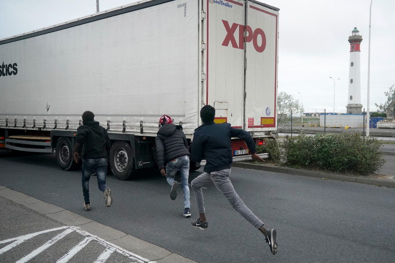 Migranţi ilegali aleargă spre un TIR în încercarea de a trece din Franţa în UK.