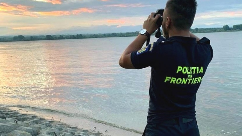 un politist de frontiera se uita cu binoclul pe malul dunarii
