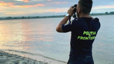 un politist de frontiera se uita cu binoclul pe malul dunarii
