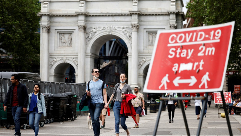 Trecători în Londra și un panou care amintește oamenilor să respecte distanțarea socială anti-Covid