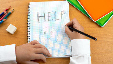 un copil care cere ajutor in scris pe un caiet