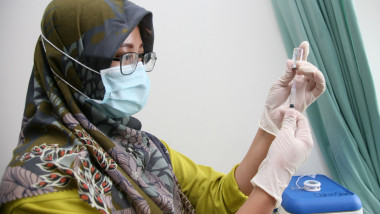 femeie medic cu batic in cap și masca la gura pregateste o seringa cu vaccin
