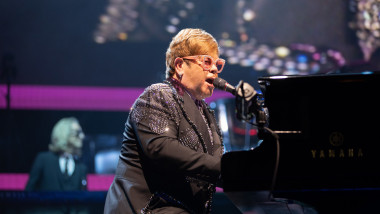 Elton John cântă la pian într-un concert.