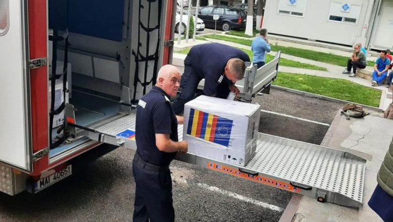 Doi angajați ai ISU descarcă mai multe cutii cu vaccinuri dintr-o mașină.
