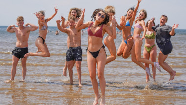 Mai mulți tineri se bucură pe plajă, lângă apă.